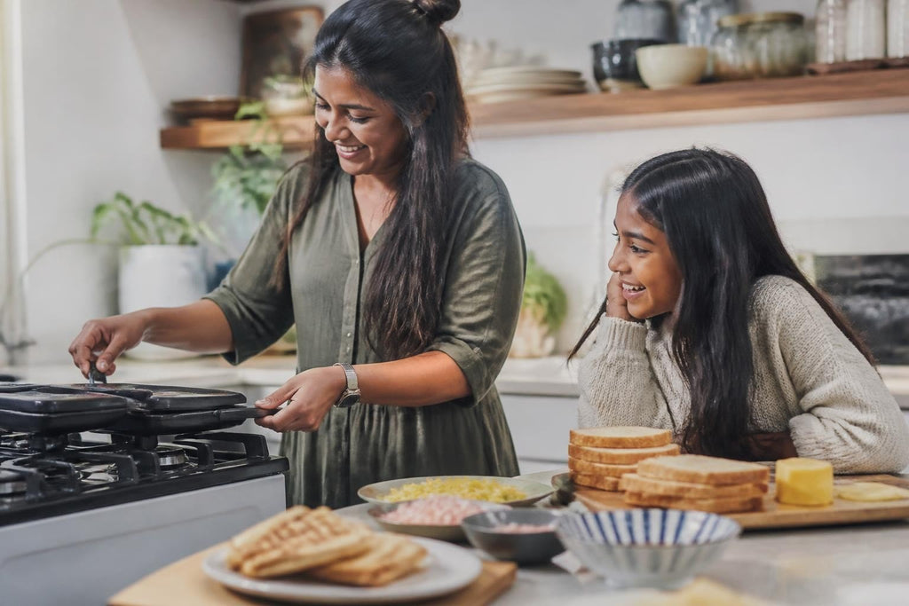 South African Comfort Food features a woman cooking on a stovetop while a girl prepares bread for sandwiches nearby.