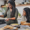 South African Comfort Food features a woman cooking on a stovetop while a girl prepares bread for sandwiches nearby.