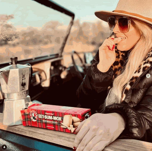 Woman enjoying Bakers Eet-Sum-Mor shortbread biscuits from a red box inside a car with a coffee maker nearby