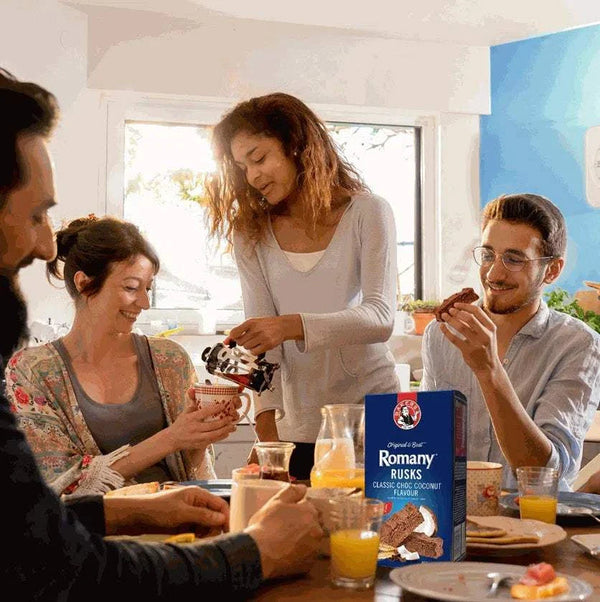 Bakers Romany Classic Choc Coconut Flavour Rusks 450g on a breakfast table with people enjoying snacks and drinks.