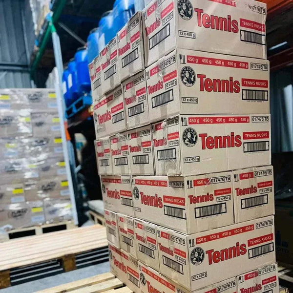 Stacks of Bakers Tennis Classic Coconut Rusks boxes in a warehouse setting.