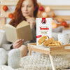 Bakers Tennis Classic Coconut Rusks 450g with woman reading, cozy setting, focus on rusks box.