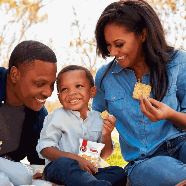 Family enjoying Bakers Tennis Mini Classic Coconut Biscuits outdoors with smiles