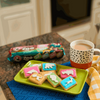 Bakers Zoo Biscuits on a green plate with colorful iced animal shapes next to a polka dot mug.