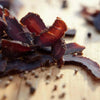 Close-up of ready-to-eat original South African biltong slices on a wooden surface with pepper seasoning, 500g pack