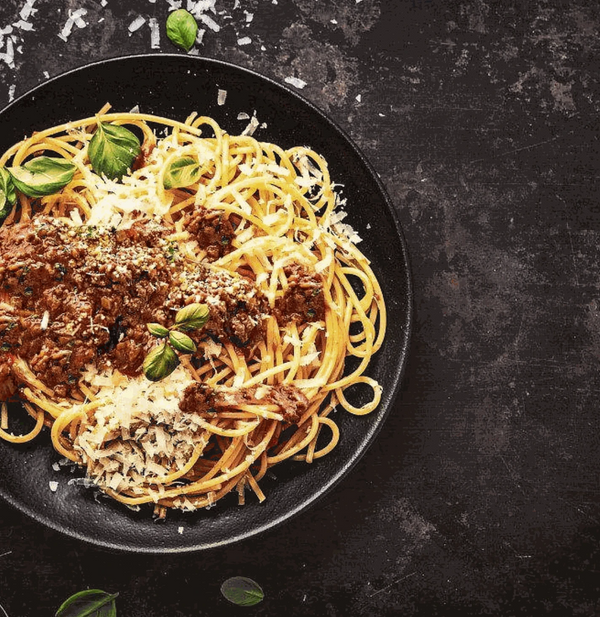 Plate of spaghetti topped with rich bolognaise sauce and garnished with fresh basil leaves and grated cheese