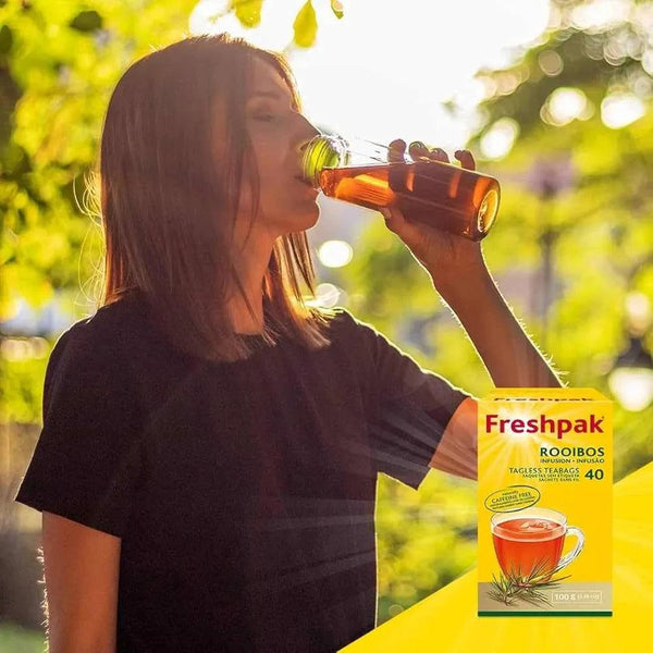 Woman drinking Freshpak Rooibos Tea outdoors with box of Freshpak Rooibos Tea 40 tagless teabags in foreground