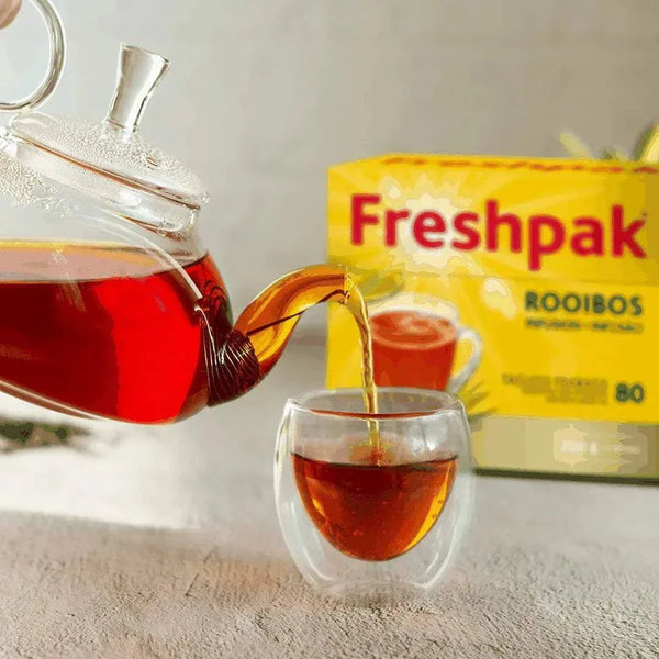 Freshpak Rooibos Tea pouring into a glass cup with vibrant red tea and Bright Freshpak Rooibos Tea 80's box in background