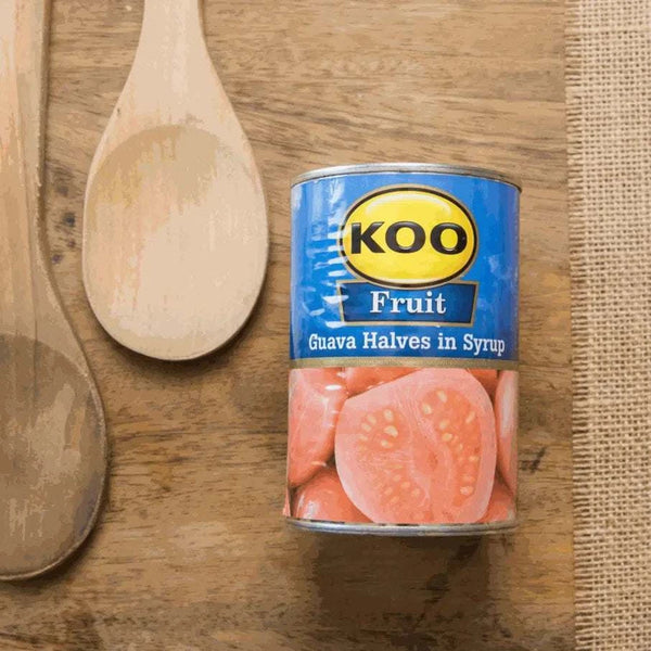 Koo Guava Halves in Syrup can on wooden table with spoons.