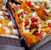 Boxes of nachos topped with melted cheese, jalapenos, diced tomatoes, and drizzle sauce.