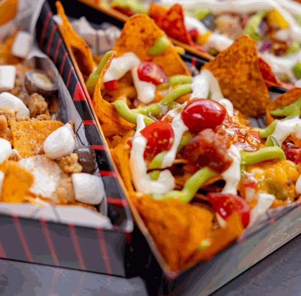 Boxes of nachos topped with melted cheese, jalapenos, diced tomatoes, and drizzle sauce.