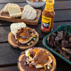 Jan Braai Basting Prego sauce bottle with grilled meat sandwiches and bread on wooden table