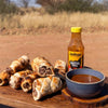 Jan Braai Prego Sauce bottle with grilled meat rolls and dipping sauce on wooden board outdoors