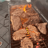 Grilled meat on a barbecue, flames visible through metal grates.
