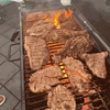 Grilled meat on a barbecue, flames visible through metal grates.