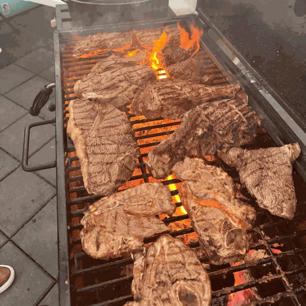 Grilled meat on a barbecue, flames visible through metal grates.