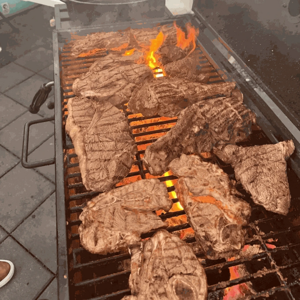 Grilled meat on a barbecue, flames visible through metal grates.