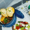 Blue 3-legged cast iron pot with stew and dumplings, featuring a handle and lid, perfect for outdoor cooking.