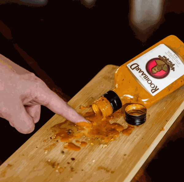 Rooibaard Original Sauce 250ml bottle spilled on wooden board.