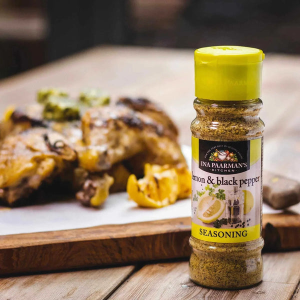 Ina Paarman Lemon & Black Pepper seasoning bottle on wooden surface with roasted chicken.