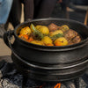 Cast-iron potjie with a black three-legged pot cooking meat, potatoes and herbs, Potjie: South African Slow-Cooked Tradition