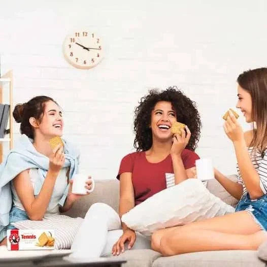 Three women enjoying Bakers Tennis Biscuits on a cozy sofa, highlighting social moments with the classic South African treat.