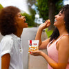 Two women enjoying Bakers Tennis Mini Classic Coconut Biscuits outdoors with pack of 5 biscuits shown