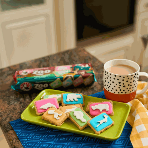 Bakers Zoo Biscuits on a green plate with colorful iced animal shapes next to a polka dot mug.