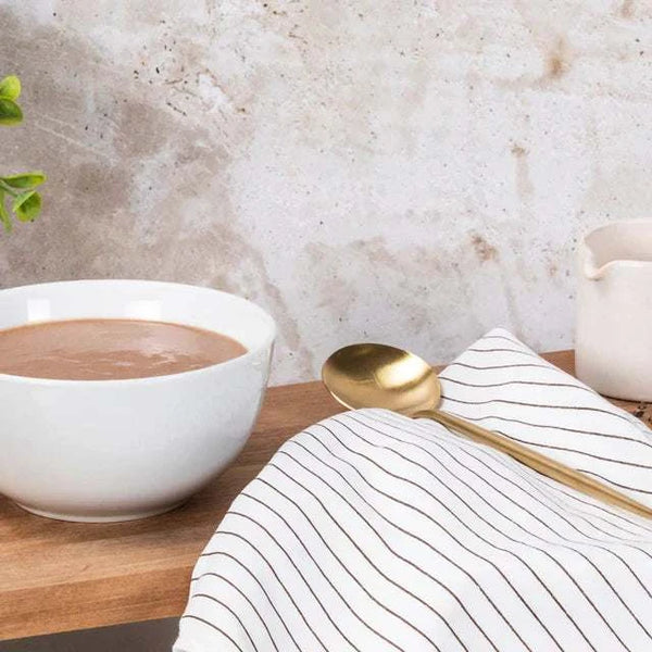 Chocolate Futurelife Zero Smart Food in a white bowl on a wooden surface, next to a striped cloth and a gold spoon.