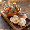 bowl of braai chicken stew with vegetables served with crusty bread rolls on wooden tray outdoors