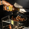 Jan Braai Basting Original sauce being poured over grilled meat in a pan for a caramelized finish