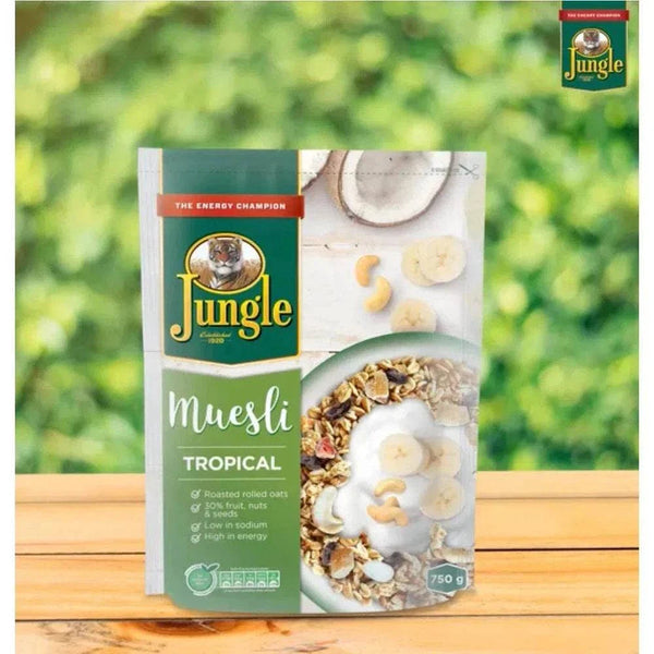 Jungle Muesli Tropical 750g pack on wooden surface with green leafy background.