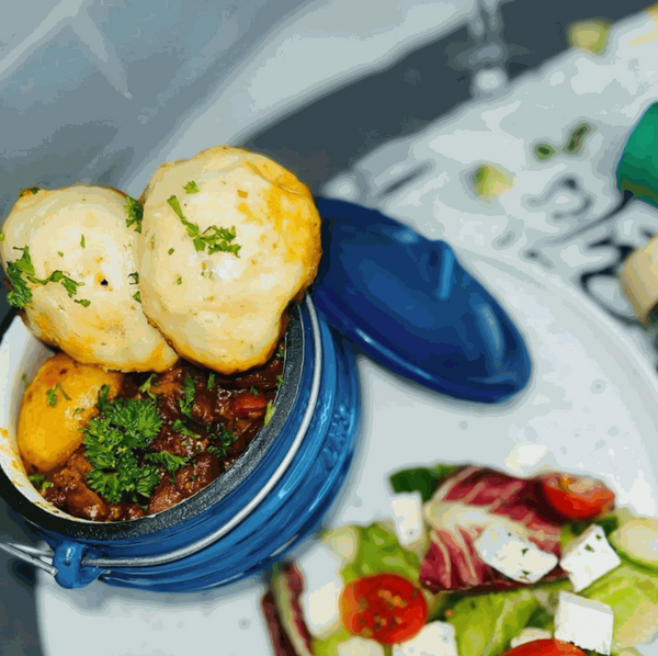 Blue 3-legged cast iron pot with stew and dumplings, featuring a handle and lid, perfect for outdoor cooking.