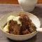 Sticky Malva Pudding with apricot butter glaze served with custard in a bowl.