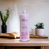 Oh So Heavenly Classic Care Body Lotion Wrapped In Romance 1L bottle on wooden surface with plants in background.