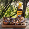 Jan Braai Basting Sauce bottle with grilled meat sliders topped with barbecue sauce on wooden board outdoors