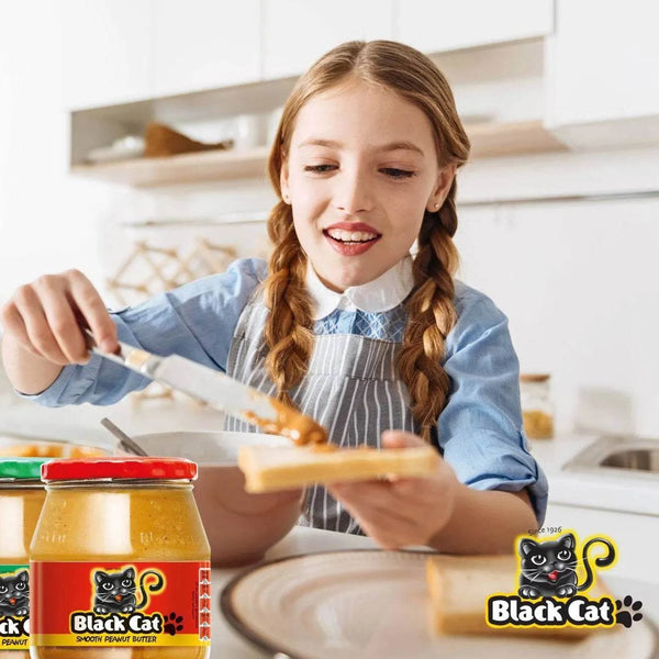 Black Cat Peanut Butter - Smooth 400g being spread on toast by a smiling person in a kitchen setting.